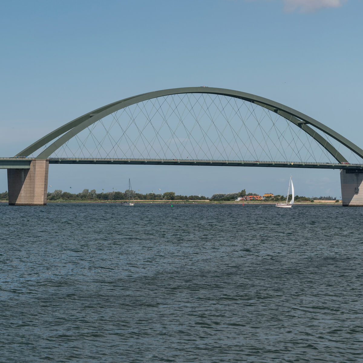 Fehmarnsundbrücke über dem Wasser mit Uferlandschaft und blauem Himmel